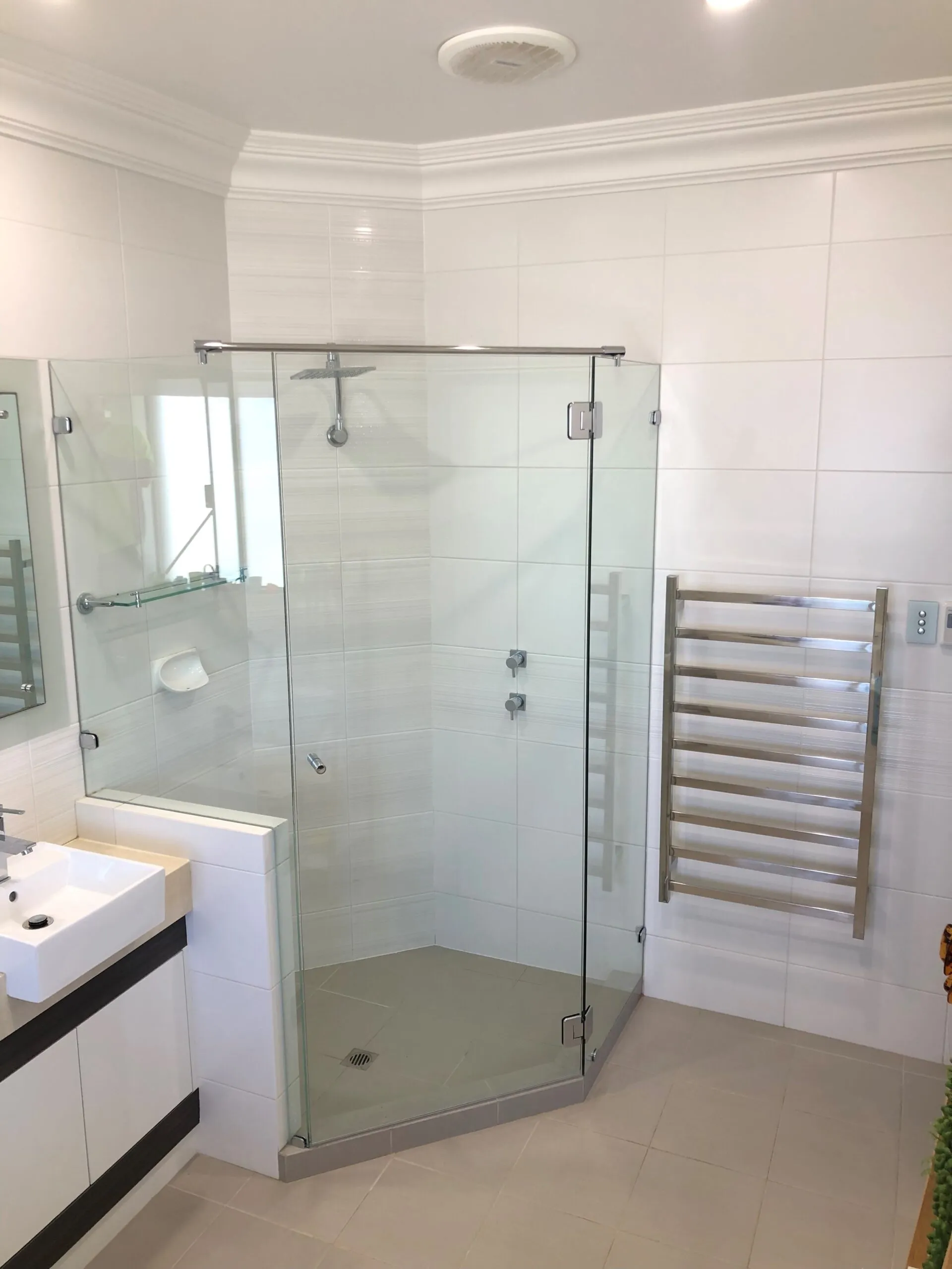 A frameless corner shower screen in a white tiled bathroom