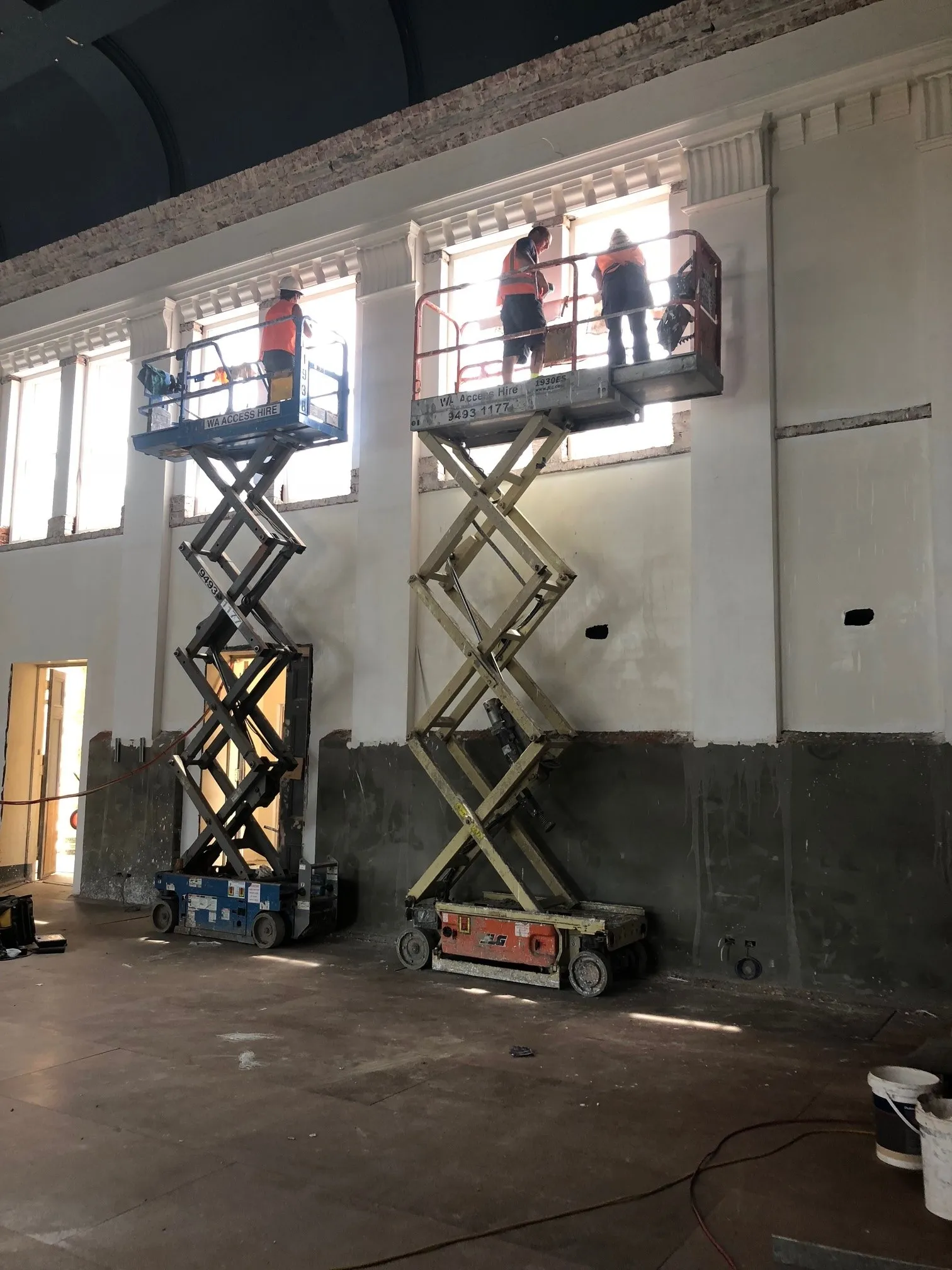 Glaziers on scissor lifts fitting high windows inside a commercial building
