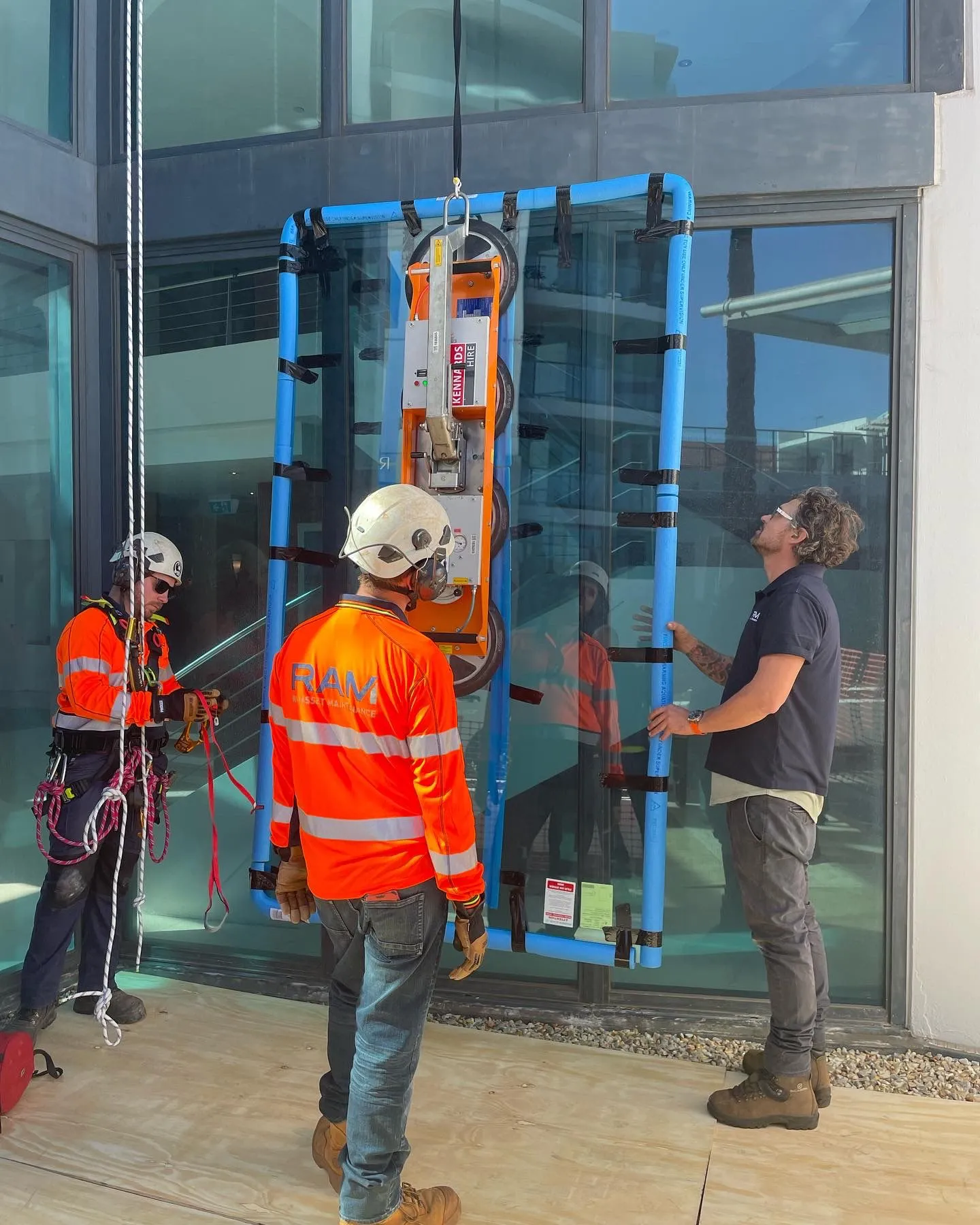 Glaziers in high-visibility gear lifting a glass panel