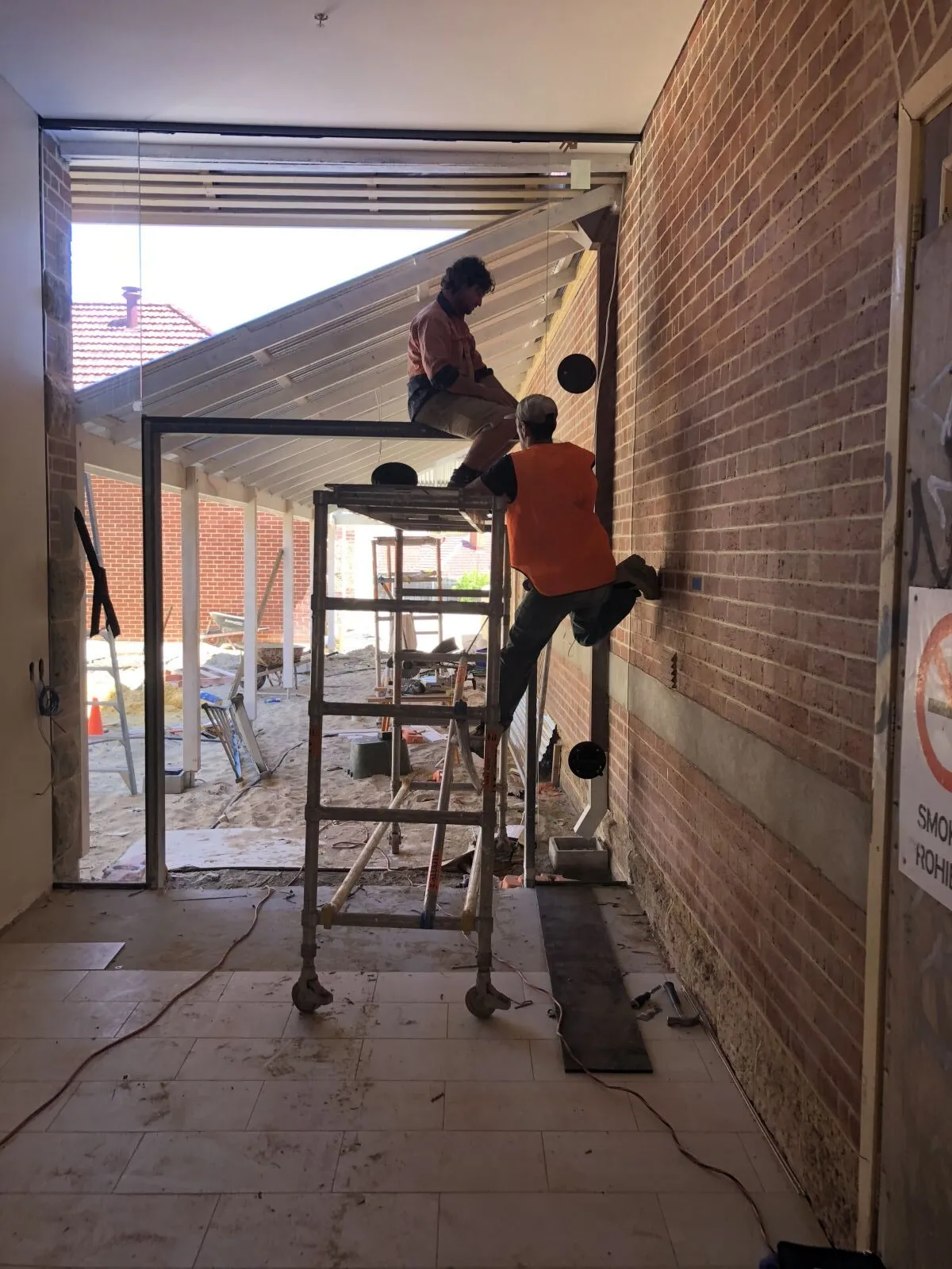 Glaziers on a scaffold fitting glass beside a brick wall