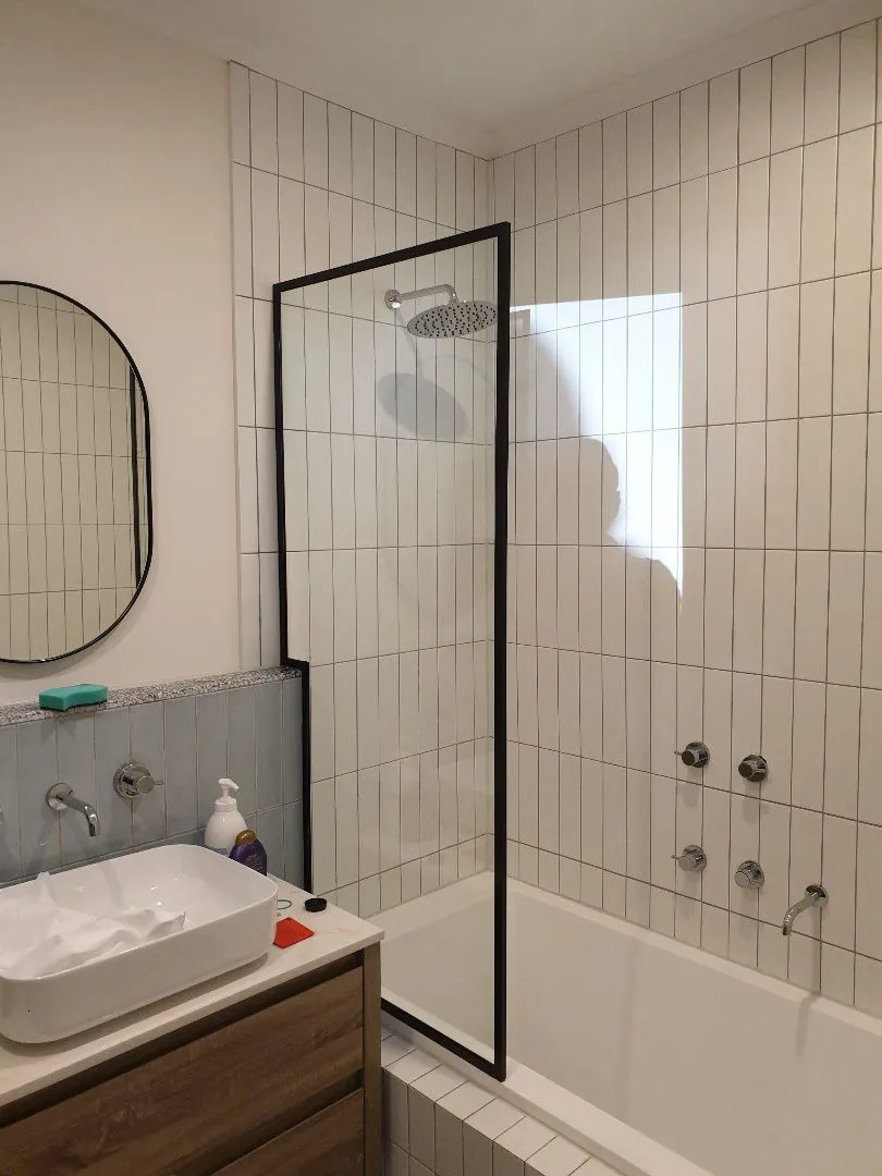Black framed shower screen over a white tiled bath